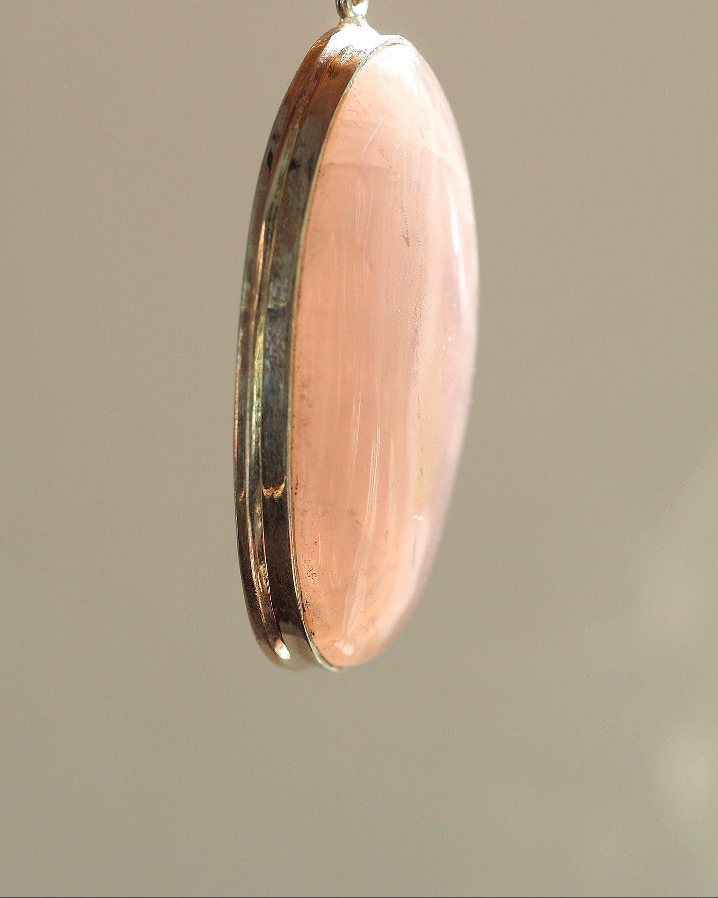 Side profile of rose quartz pendant showing domed stone height above bezel and light bezel wear