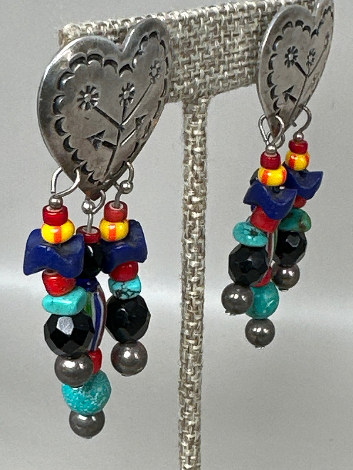 Side angle of Taxco heart earrings showing stamped floral cutwork and beaded strands with turquoise and chevron beads