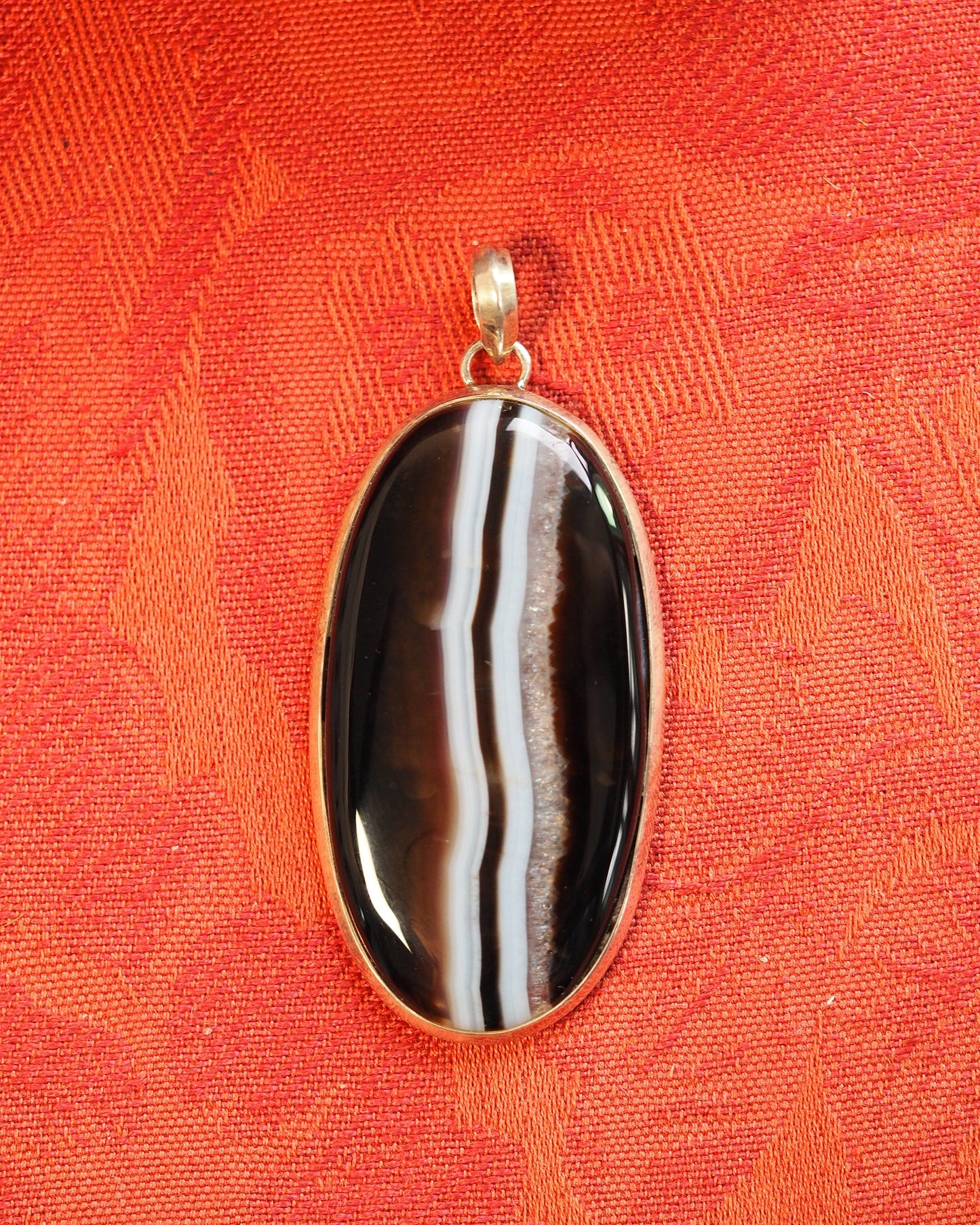 Banded agate pendant in silver bezel on orange fabric, front view showing vertical black, brown, white stripes