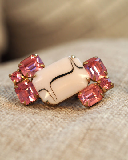 Close-up of one earring showing the emerald-cut pink rhinestones and black-line detail on the white cabochon
