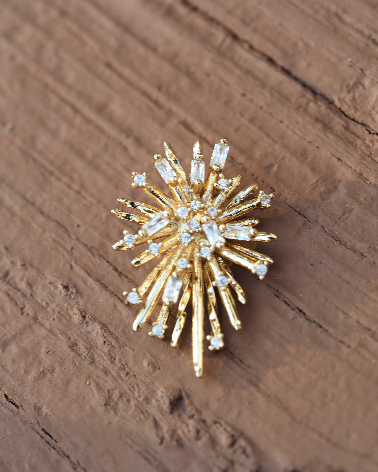 Single starburst earring front view, detail of alternating smooth gold rays and baguette/round rhinestone settings