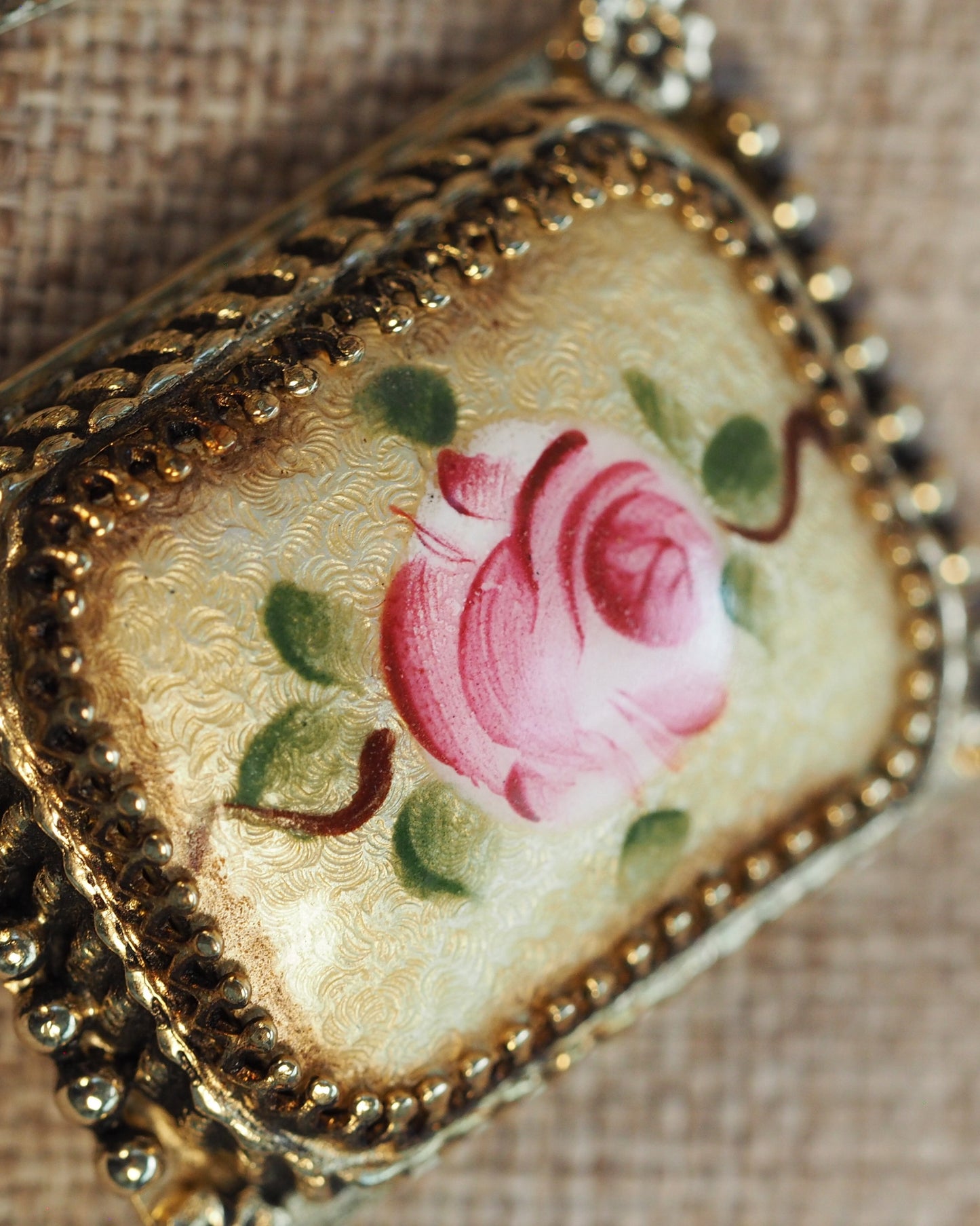 Close-up of one earring showing the hand-painted pink rose on cream-and-gold guilloché background with beaded trim detail