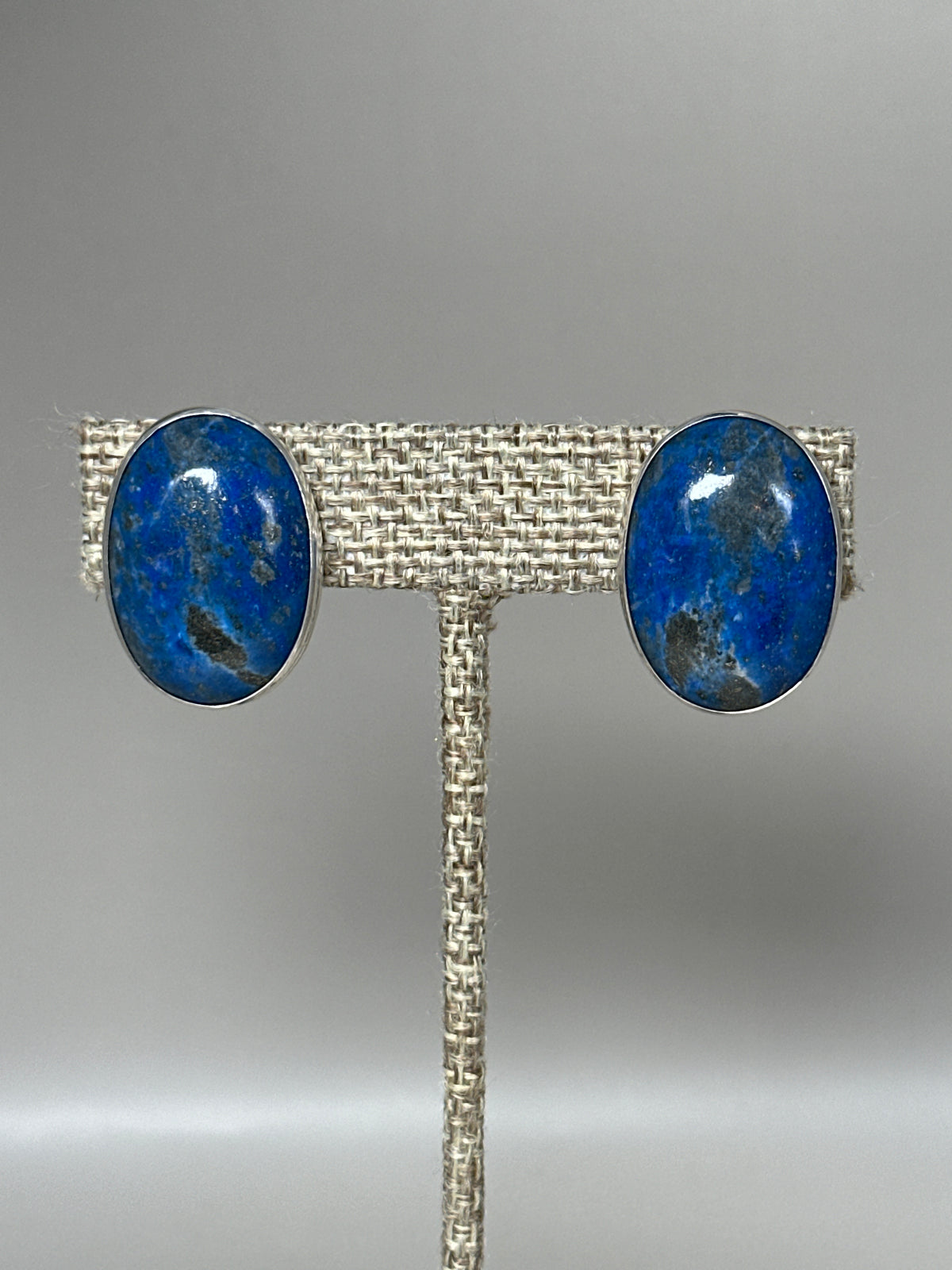 Sterling silver clip earrings with large oval blue lapis lazuli cabochons, front view on earring stand
