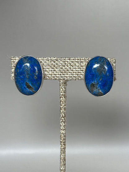 Sterling silver clip earrings with large oval blue lapis lazuli cabochons, front view on earring stand