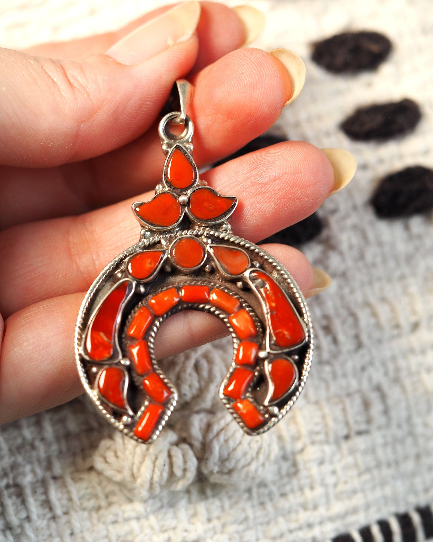 Silver naja pendant with red coral inlay held in hand, front view showing horseshoe crescent and three-petal cluster