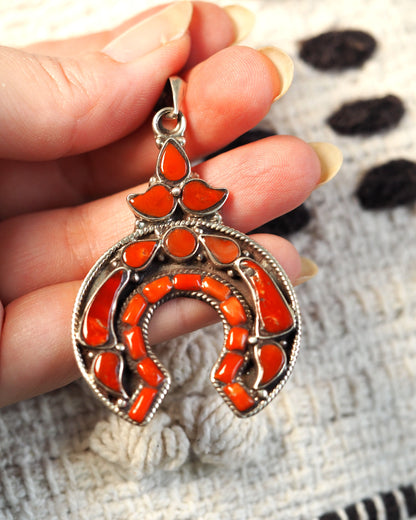 Silver naja pendant with red coral inlay held in hand, front view showing horseshoe crescent and three-petal cluster
