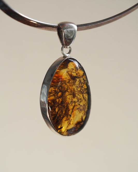 Sterling silver amber pendant with large freeform cabochon showing golden yellow to cognac color gradation, front view on black cord