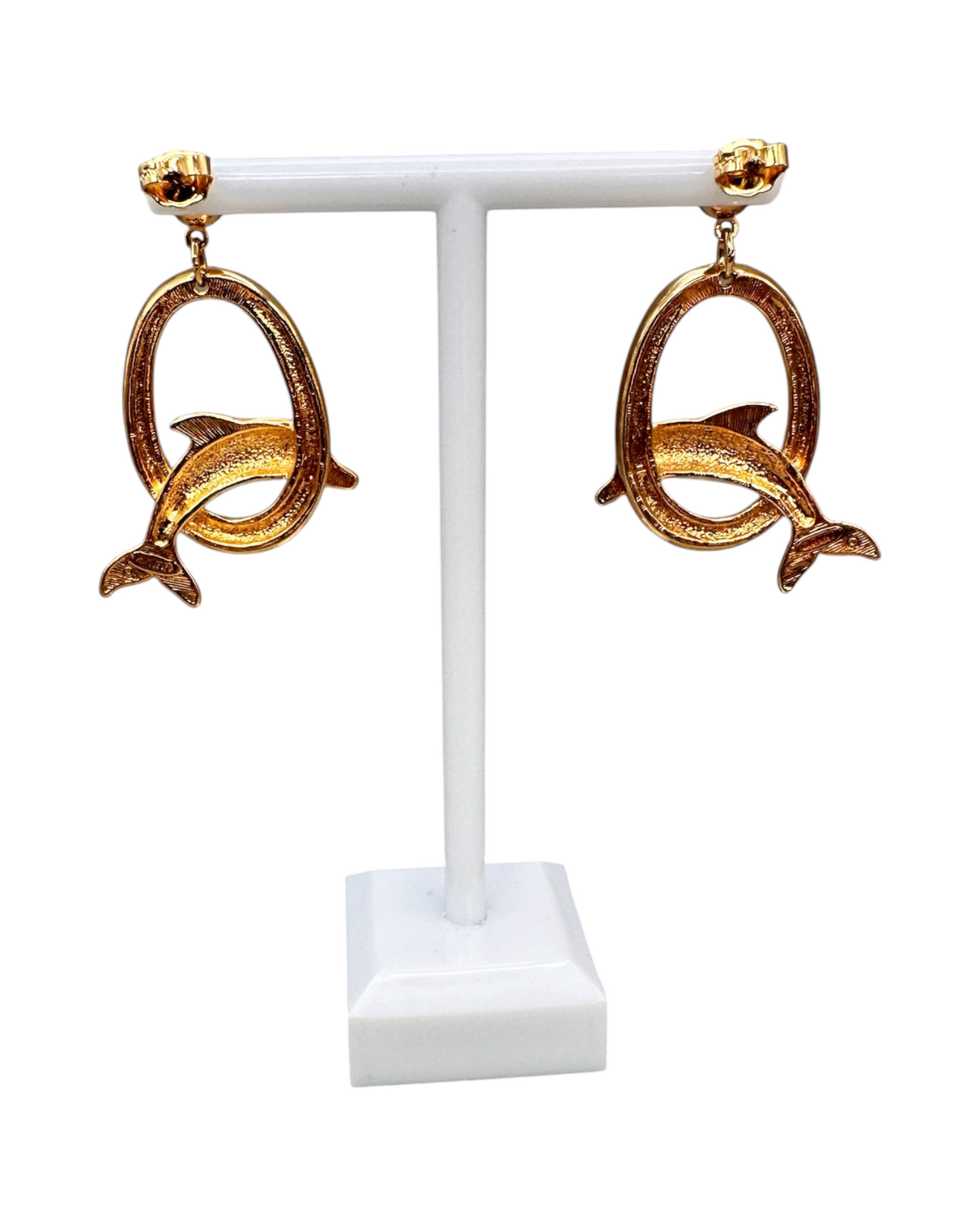Front view of pair of Avon dolphin dangle earrings on white T-bar stand showing symmetry and textured oval hoops
