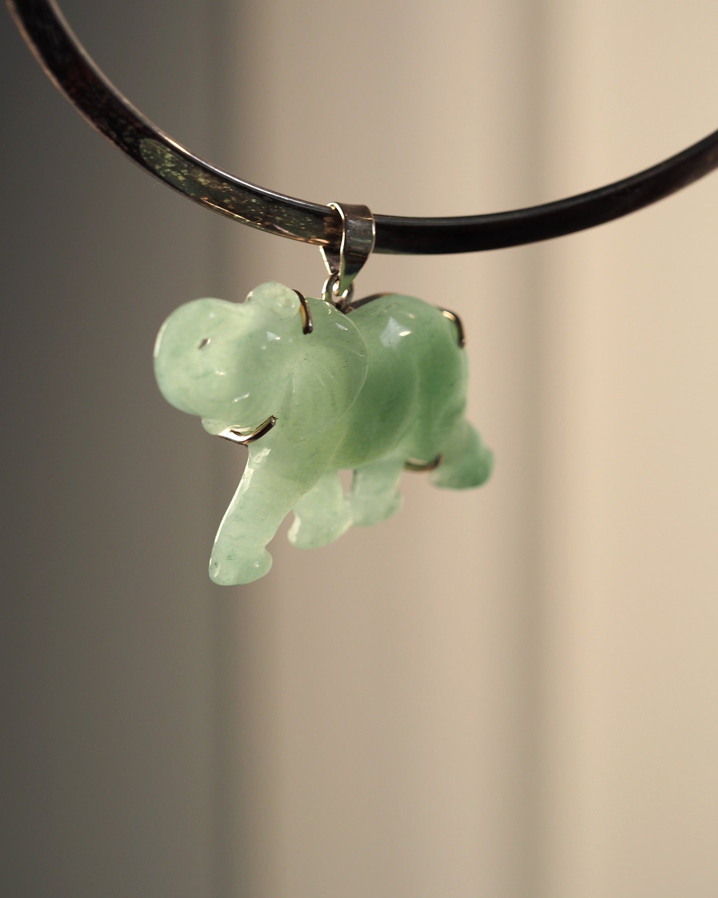 Sterling silver aventurine elephant pendant hanging from black cord, front view showing raised trunk and pale green translucent stone