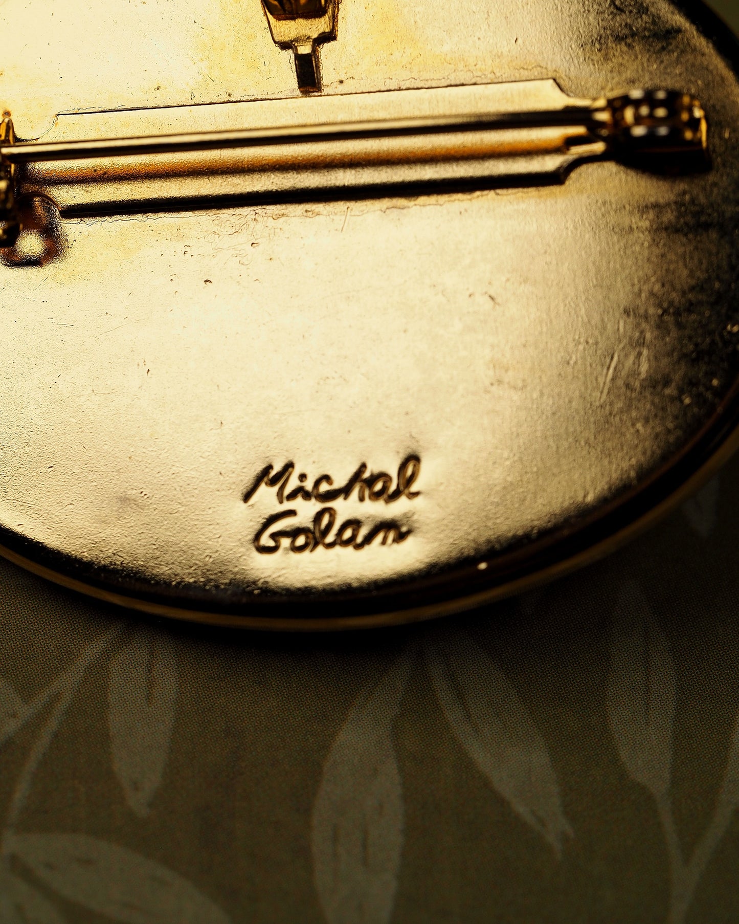 Close-up of signature 'Michal Golan' script on black enamel reverse of brooch