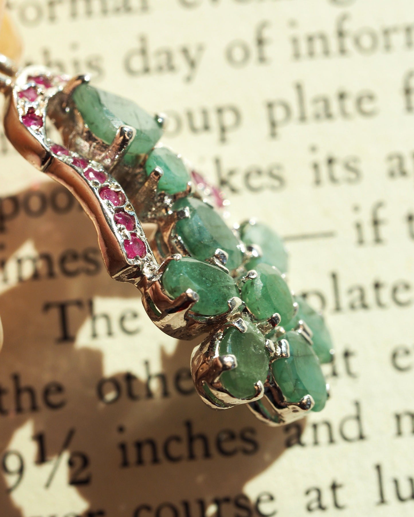 Close-up of prong-set green cabochons in a sterling silver flower motif with red accent stones