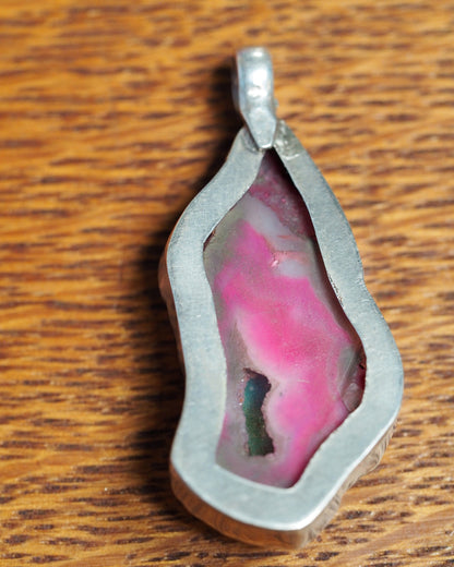 Back view of dyed pink agate slice pendant showing open-back setting and banded stone