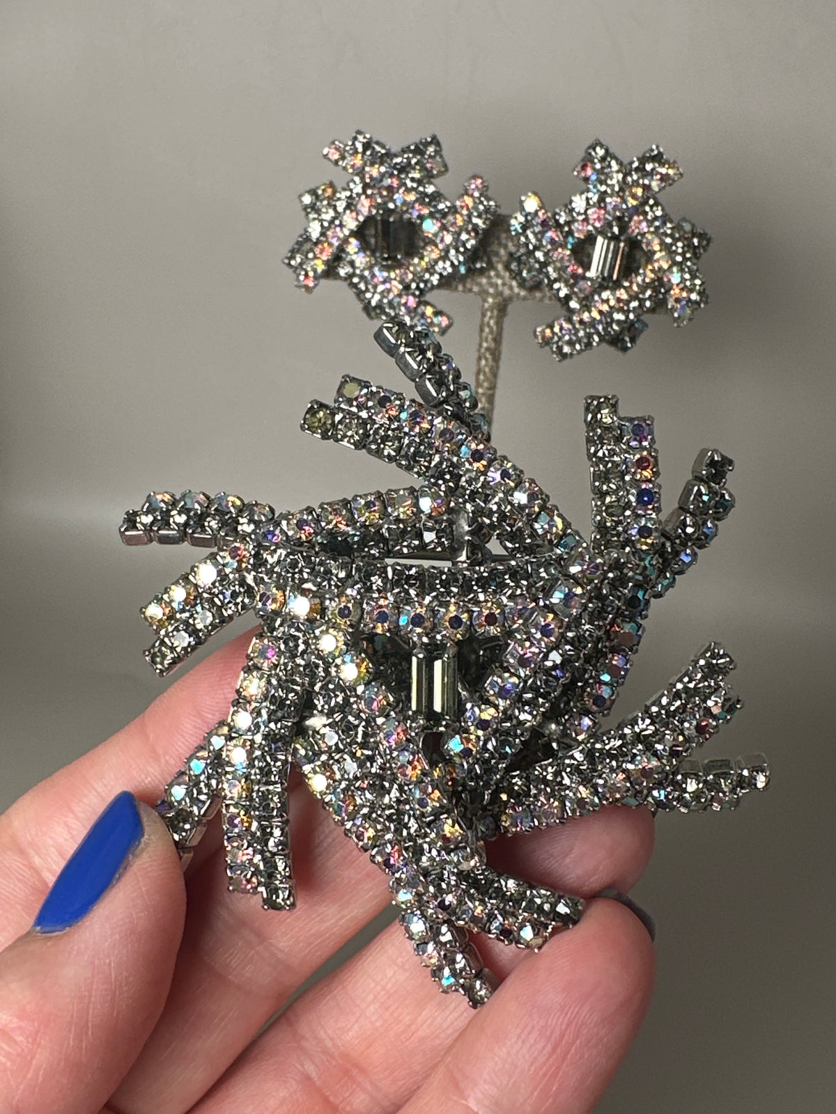 Silver-tone starburst brooch with Aurora Borealis and smoky rhinestones held in hand, front view showing sculptural radiating arms