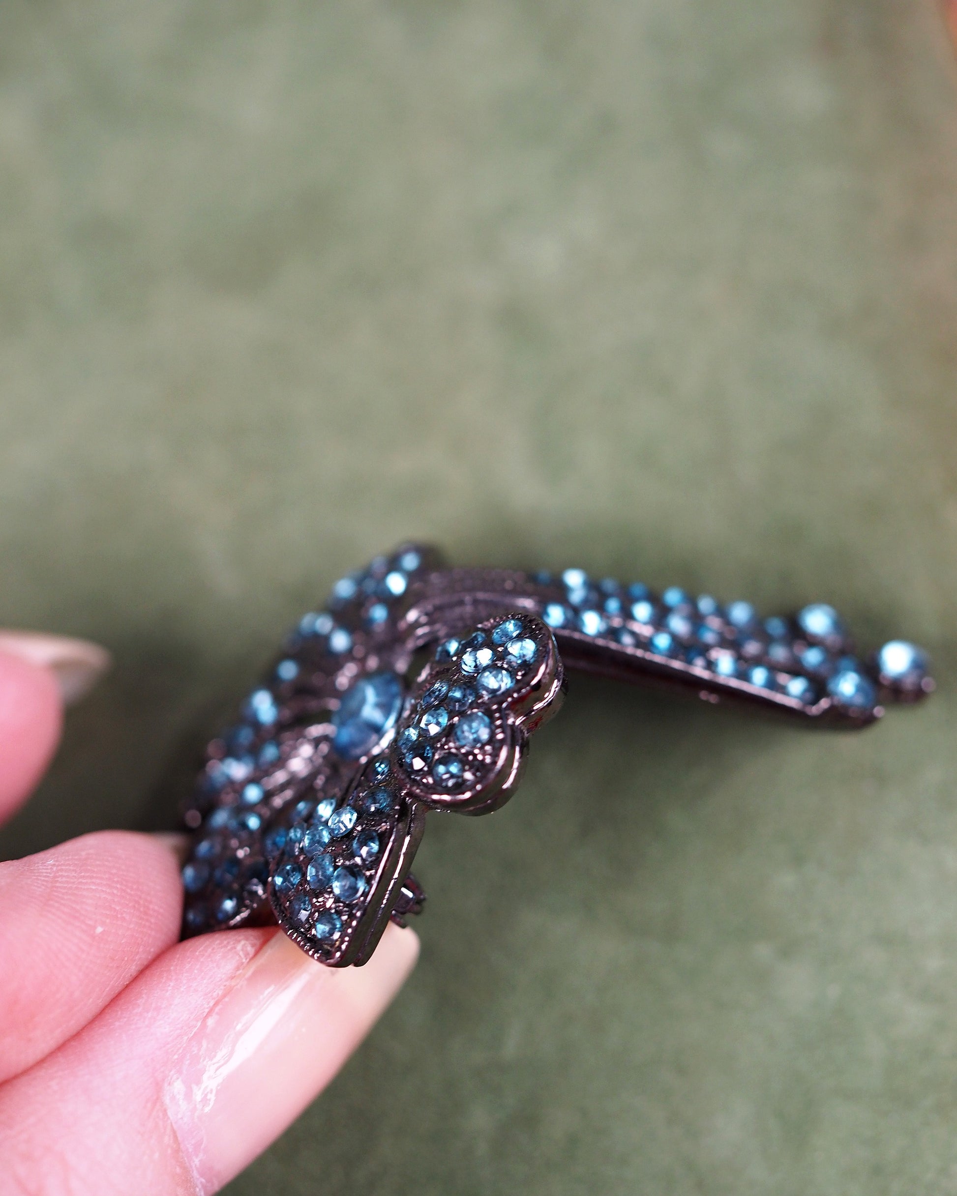 close-up of gunmetal rhinestone brooch showing articulated drop strands and channel-set teal stones