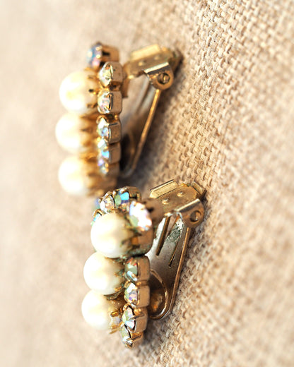 Close-up of the backs of gold-tone clip earrings showing prong-set rhinestones and clip mechanisms with visible finish wear