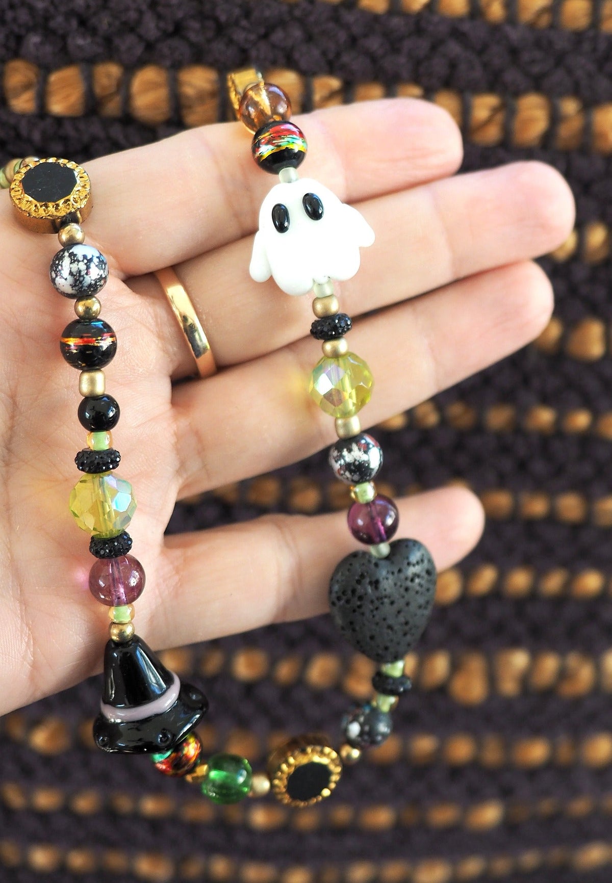 Glass bead necklace held in hand showing white ghost bead, lava stone heart, multicolor blown glass beads, and gold-tone accents for scale
