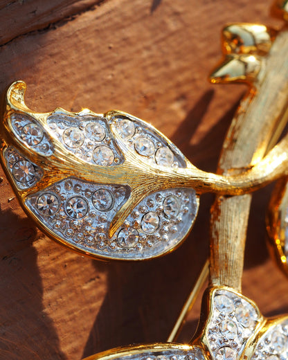 Nolan Miller rose brooch on wood, angled view showing dimensional petal construction and articulated leaves