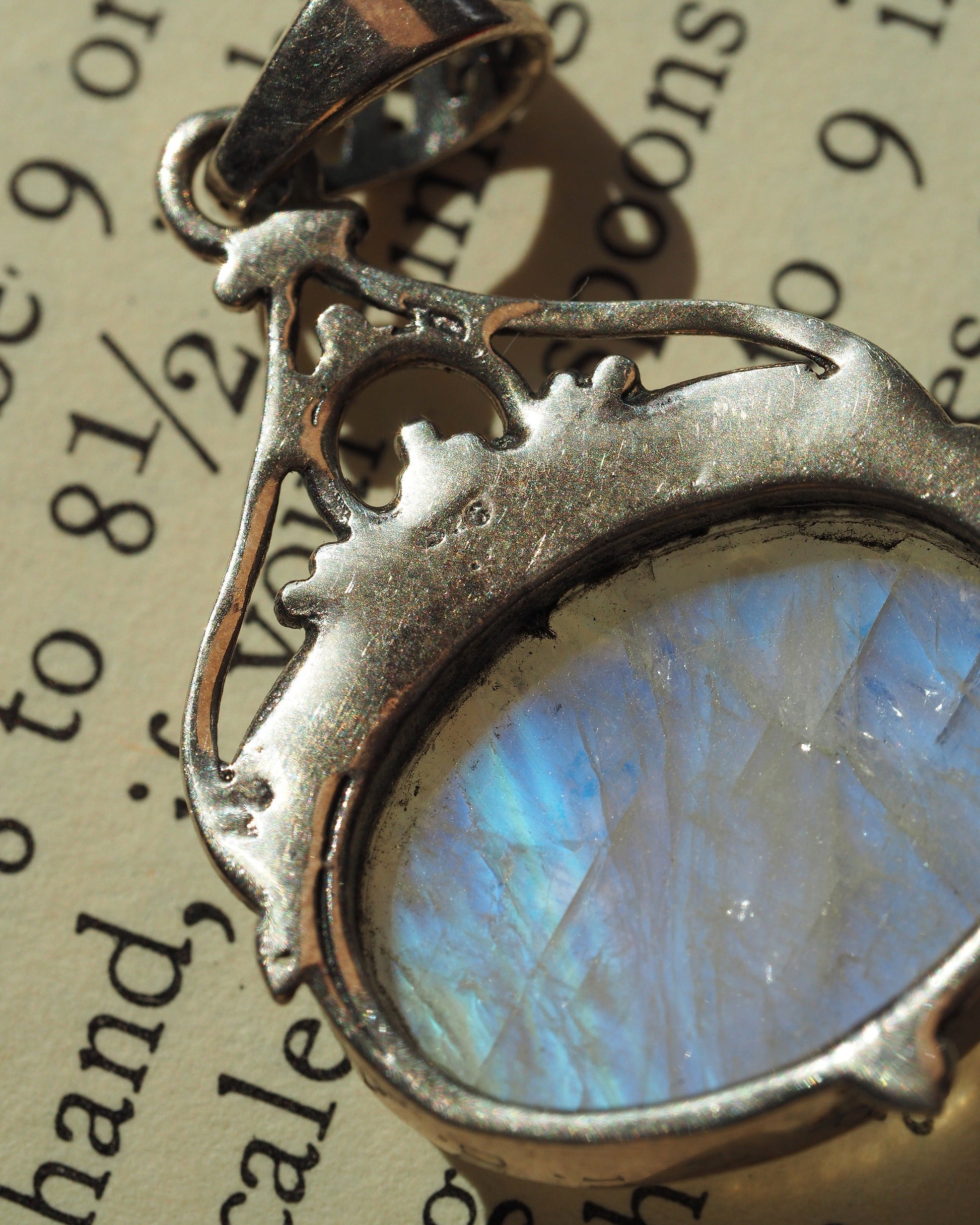 Detail of moonstone pendant filigree bail with scrollwork, beaded accents, and openwork heart cutouts in sterling silver