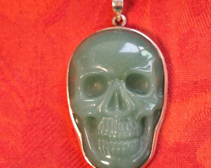 Aventurine skull pendant straight-on view against red background, showing carved facial features and sterling bezel