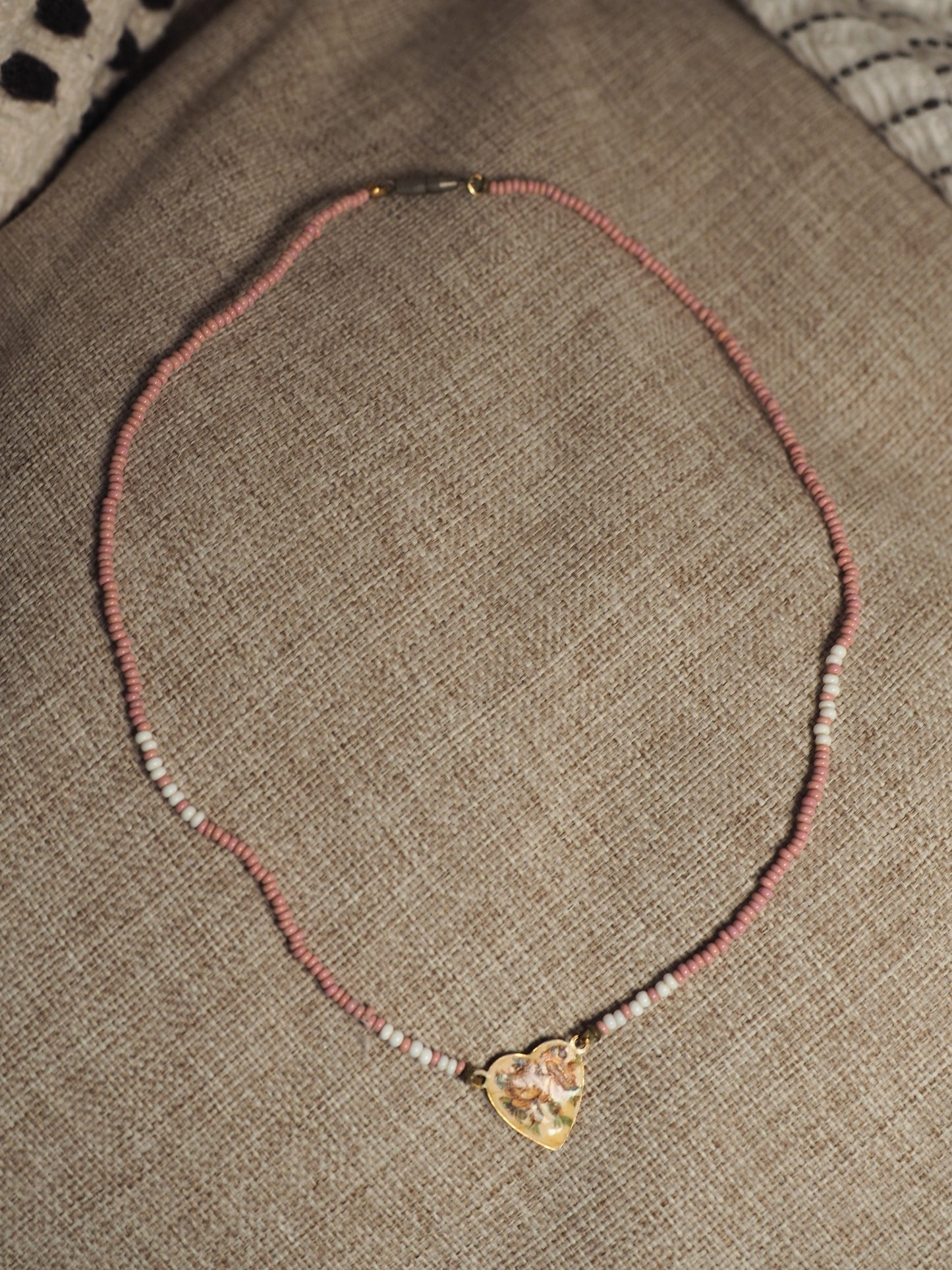 Full 16-inch necklace laid in a circle showing pink and white beaded strand with brass heart charm
