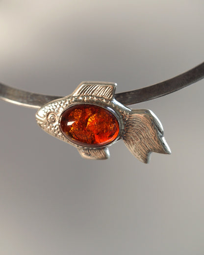 Sterling silver fish pendant with oval amber cabochon at the body center, front view on a leather cord