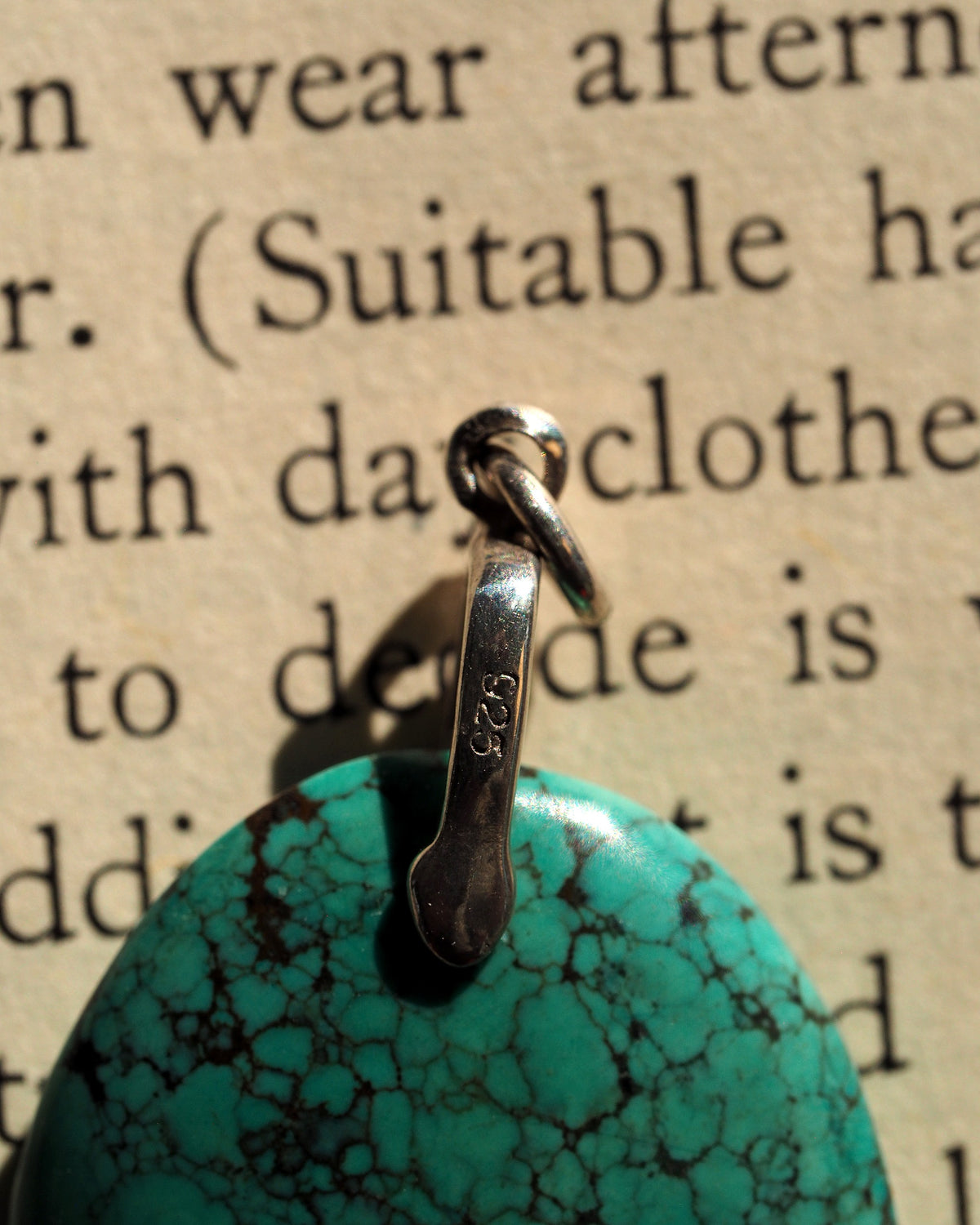 Blue-green stone pendant held on fingertip for scale, showing round shape and vivid color