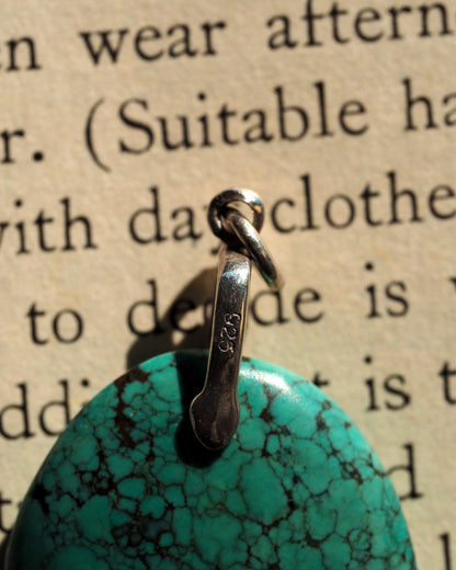 Blue-green stone pendant held on fingertip for scale, showing round shape and vivid color
