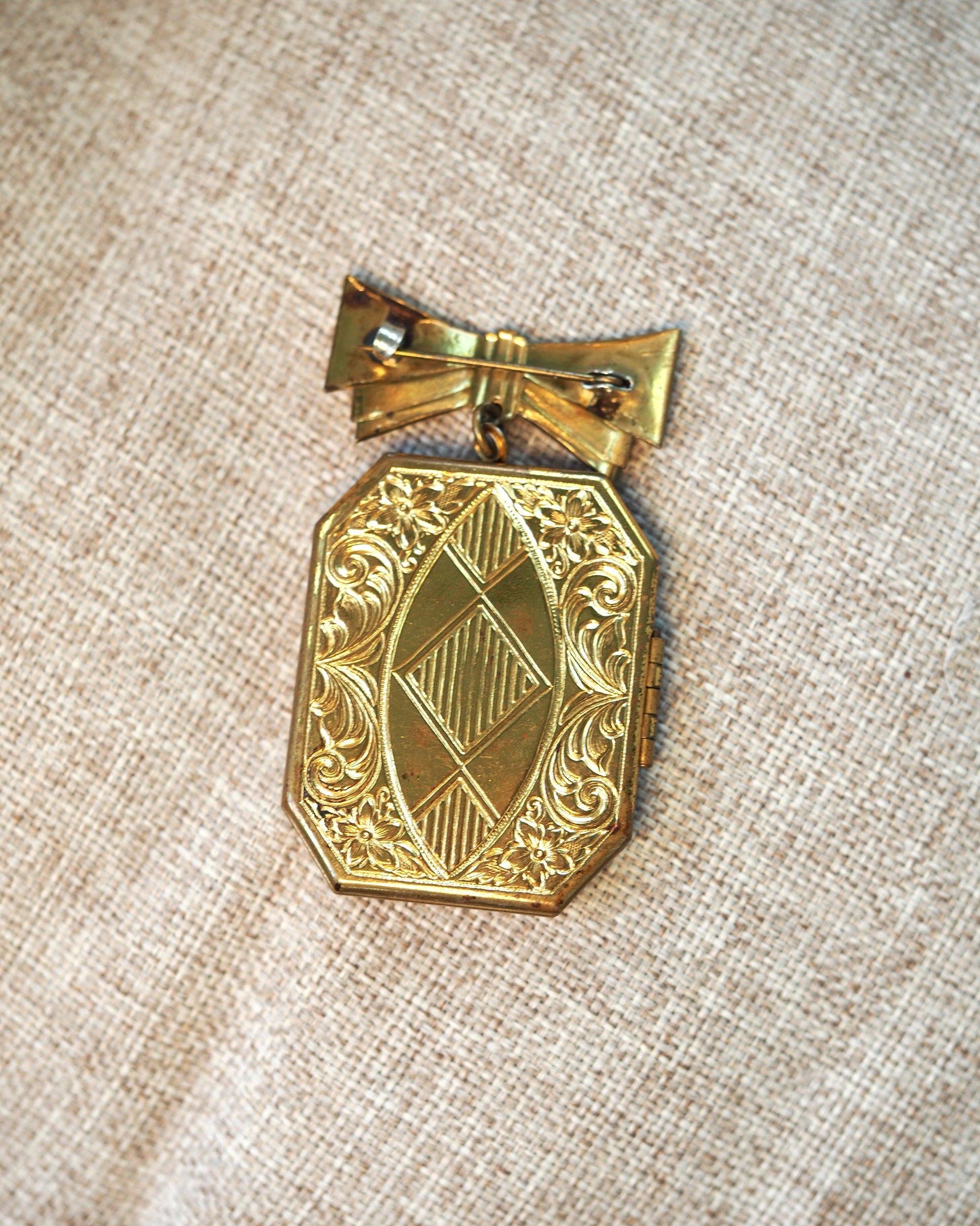 Back view of the locket brooch showing geometric engraved pattern and pin clasp