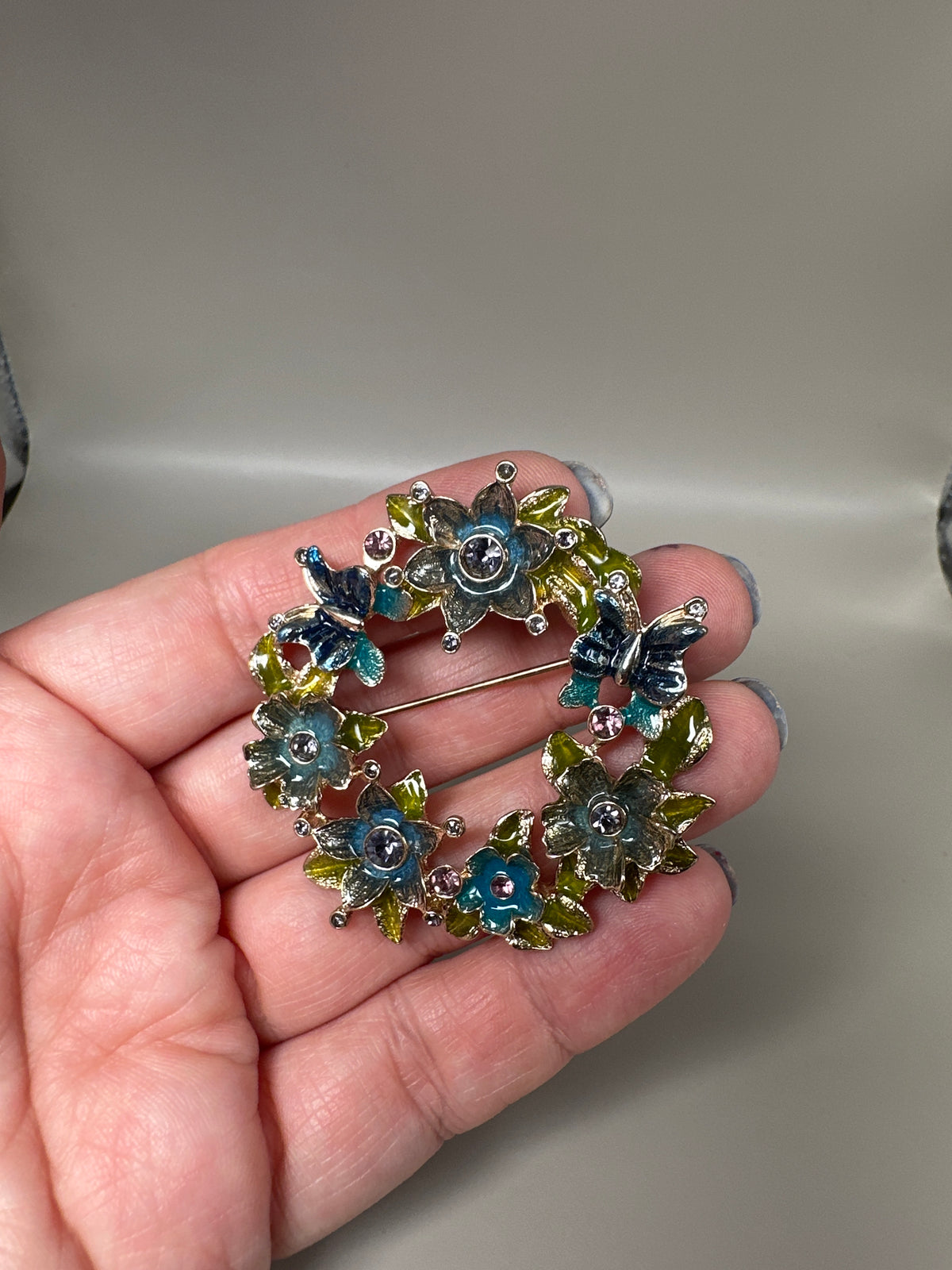 Napier enamel floral wreath brooch held in hand for scale, showing dimensional construction and multi-color enamel detail