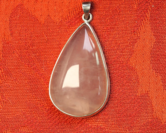 Sterling silver rose quartz teardrop pendant, light pink cabochon stone in bezel setting, front view on red background