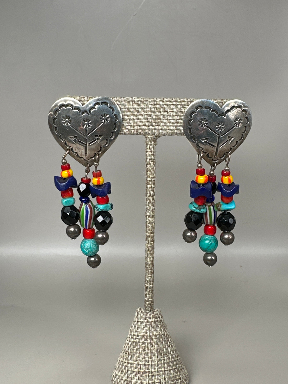 Sterling silver Taxco heart pierced earrings with turquoise-colored and glass beaded dangles, front view on stand