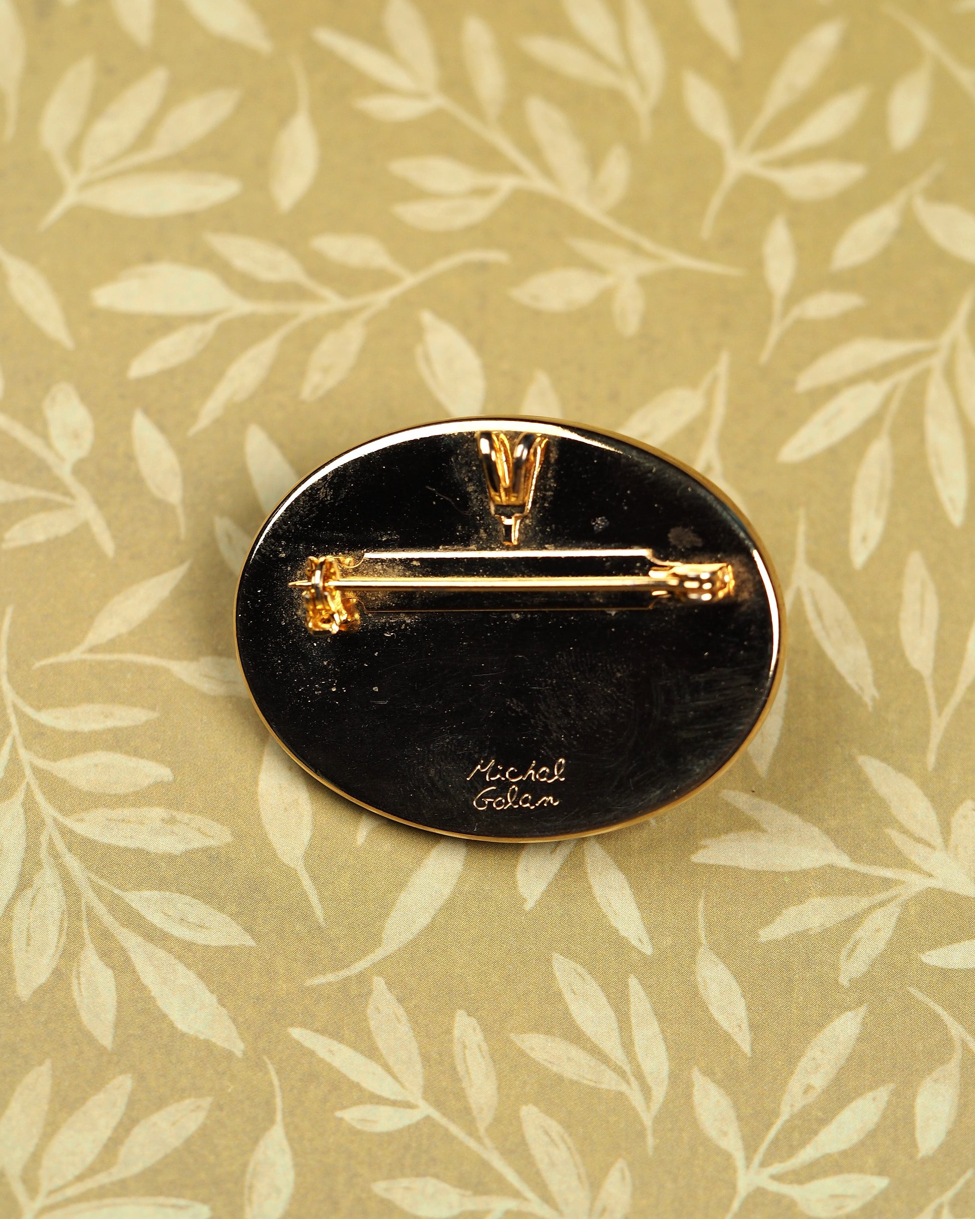 Reverse of Michal Golan brooch showing black enamel backing, engraved signature, and pin clasp