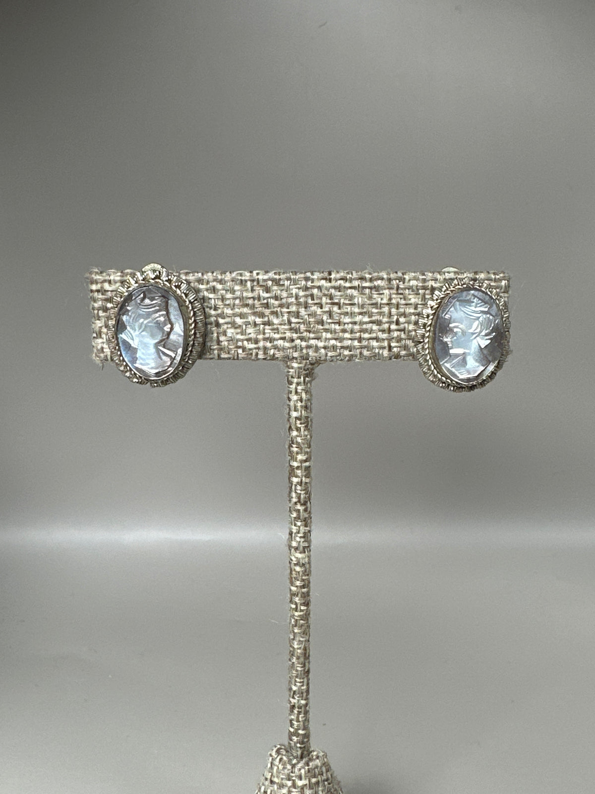 800 silver mother-of-pearl cameo clip earrings with carved profiles and notched bezel frames, front view on stand