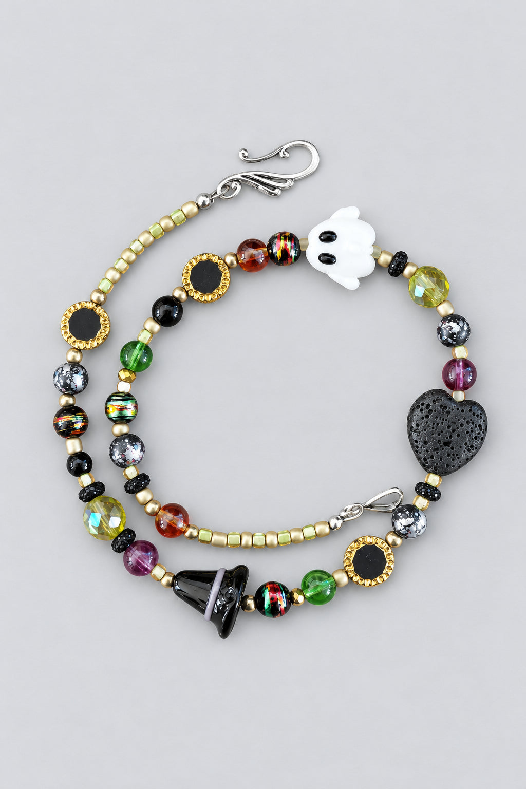 Close-up of glass bead necklace laid flat showing ghost bead, lava stone heart, gold-tone disc beads, and multicolor glass beads with silver-tone clasp