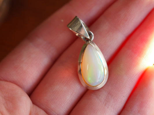 Sterling silver opalite teardrop pendant held in hand, showing luminous white stone with green and peach iridescence and fixed bail