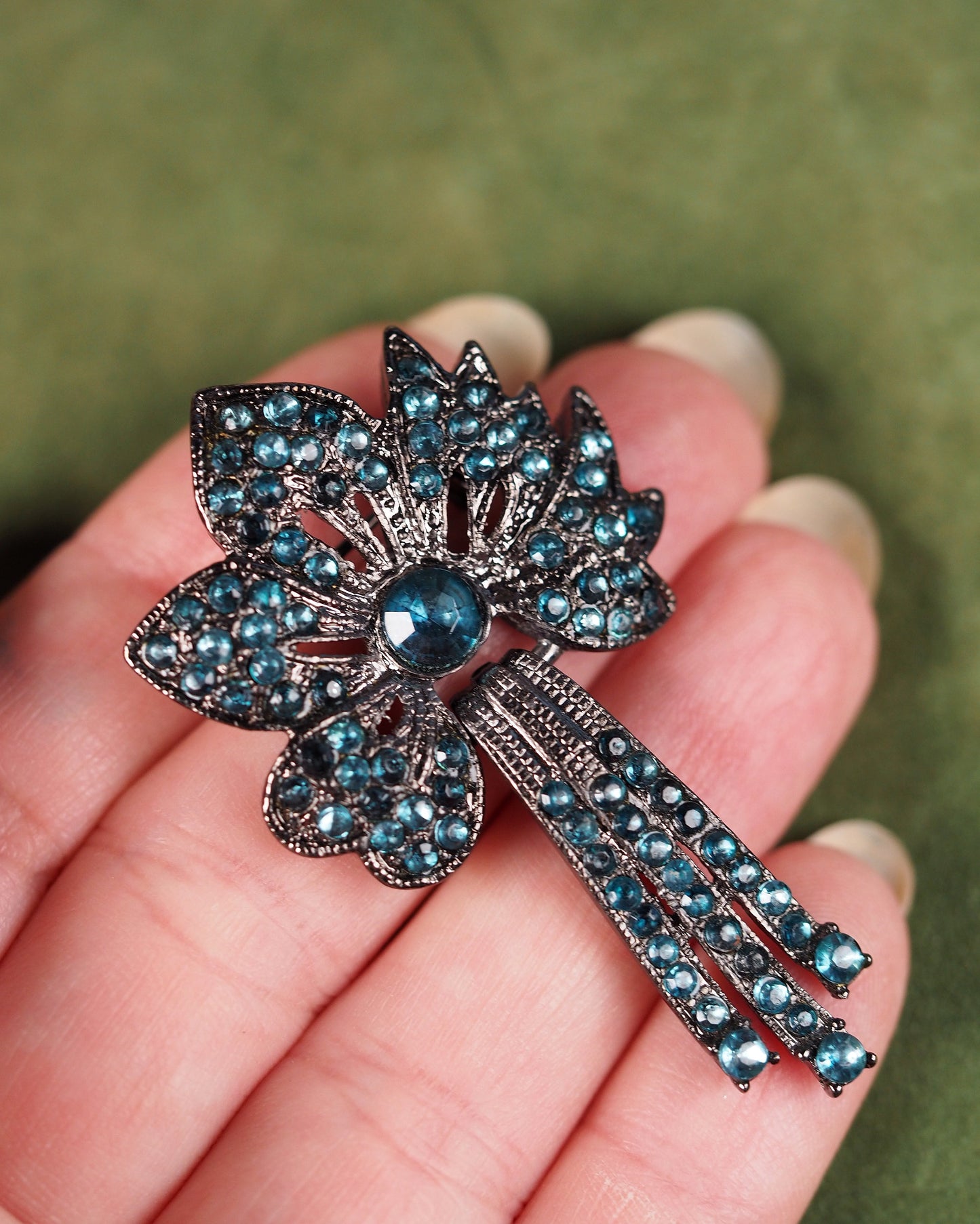 teal rhinestone flower brooch held in palm for scale, showing 1.25-inch size and articulated drop