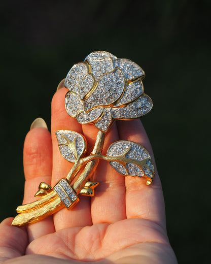 Nolan Miller gold-tone rhinestone rose brooch held in hand, front view showing layered petals and articulated leaves on brushed stem