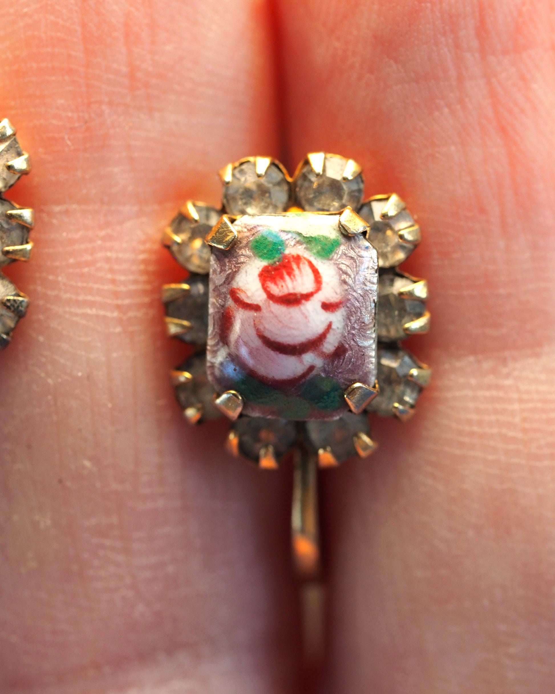 Close-up of painted glass cabochon showing red rose with green leaves on tan ground, surrounded by rhinestone halo
