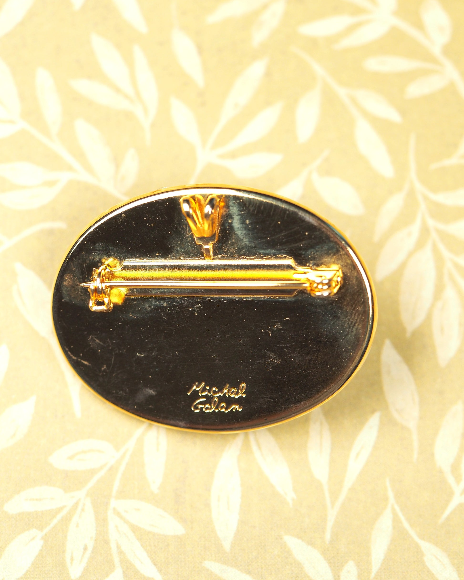 Reverse of Michal Golan brooch showing signature script on black enamel backing with gold-tone pin back