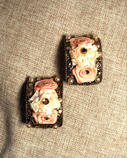 Ribbon rose clip earrings shown at an angle, revealing dimensional molded roses and filigree scrollwork detail