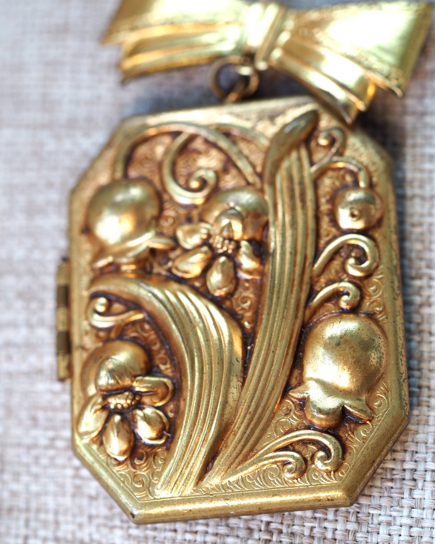 Close-up of the high-relief floral clusters, scrollwork, and flowing ribbon motif on the locket face