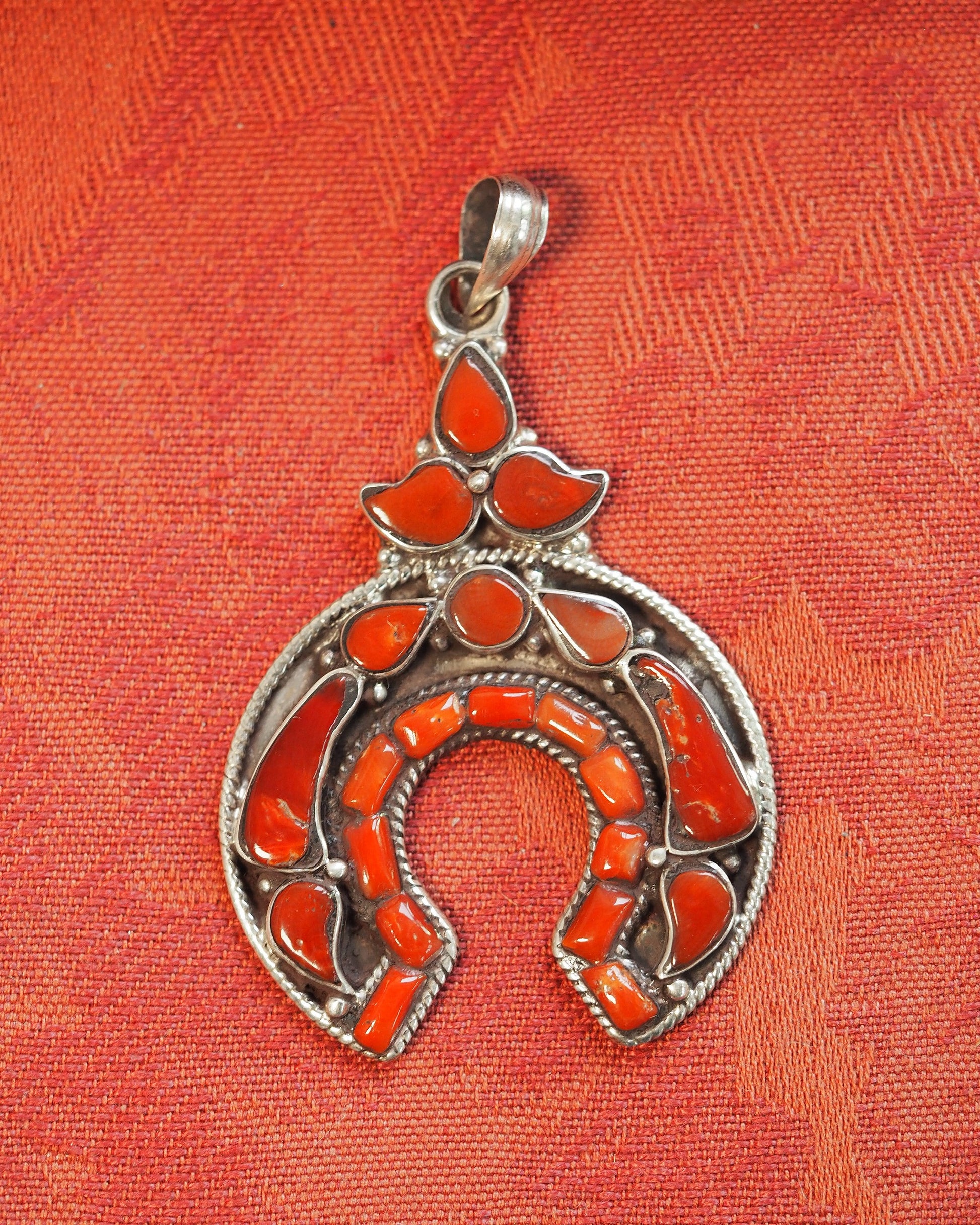 Red coral naja pendant on orange fabric, full front view showing twisted rope bezels and coral cabochons