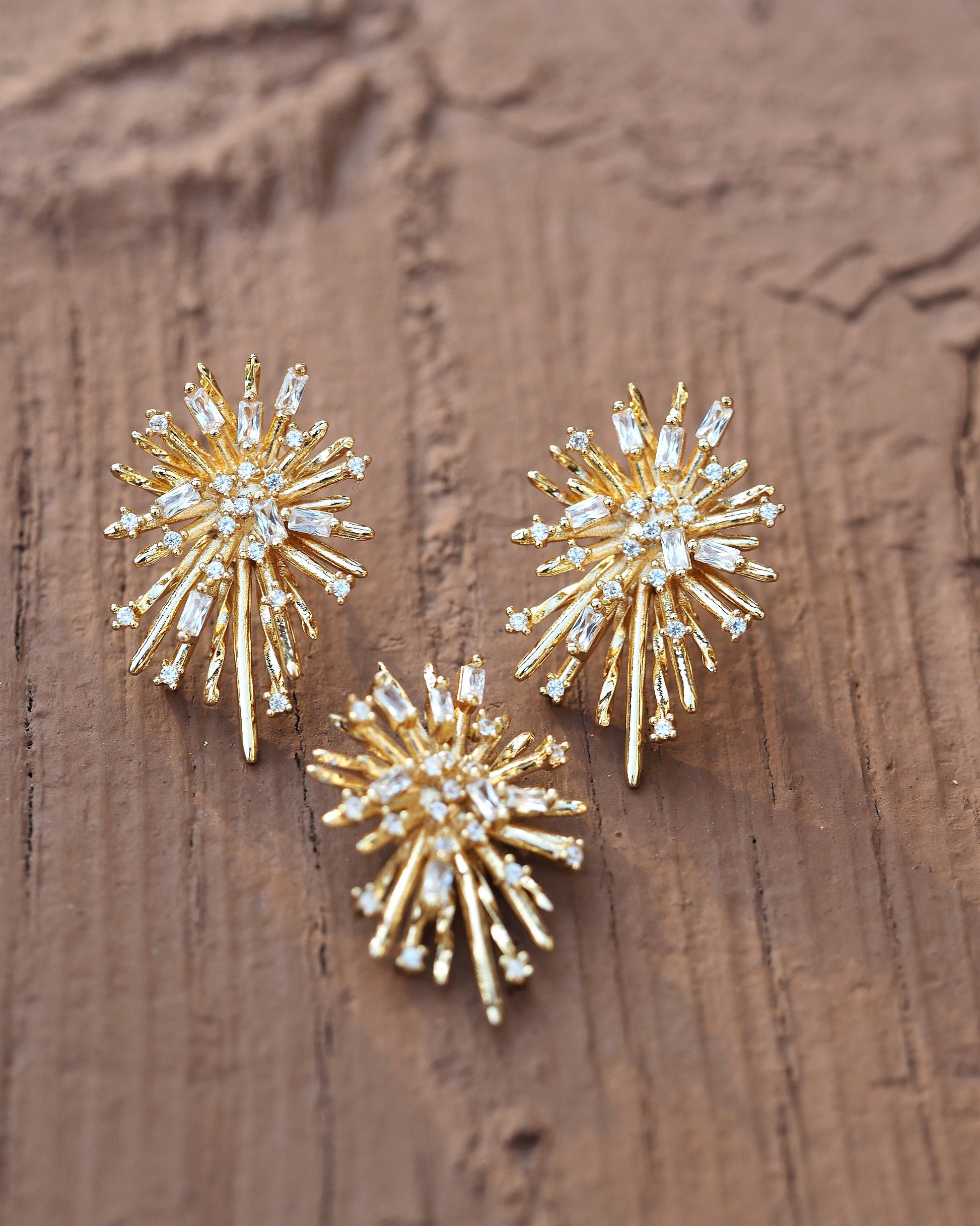 Gold plated sterling silver starburst earrings with clear rhinestones, shown with matching pendant on weathered wood, front view