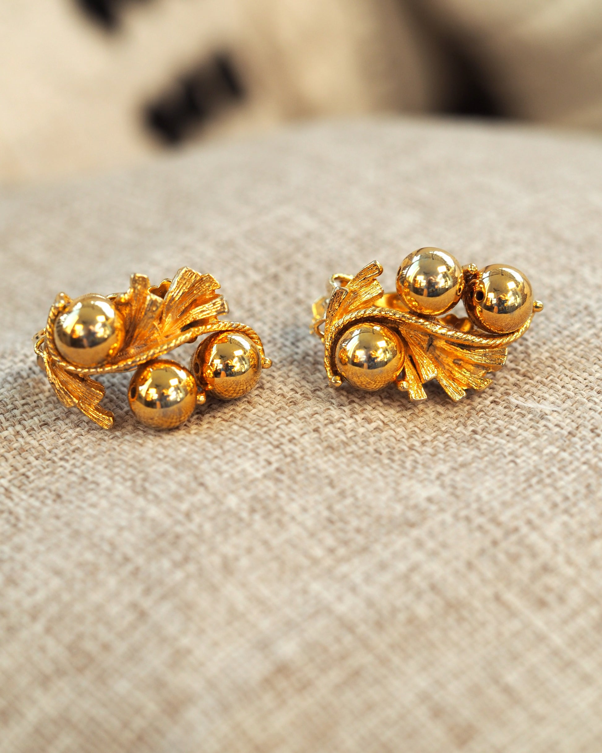 Side angle view showing the dimensional construction of the leaf and orb earrings with textured fronds and twisted rope detail