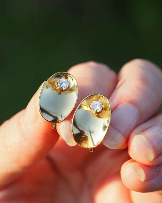 Mid-Century gold-tone oval clip earrings with crystal accent, front view on fingertips